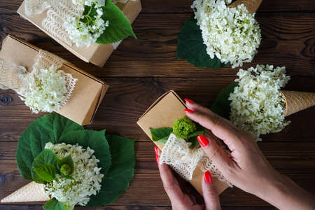 Womens hands pack a gift in a craft box with hydrangea flowers