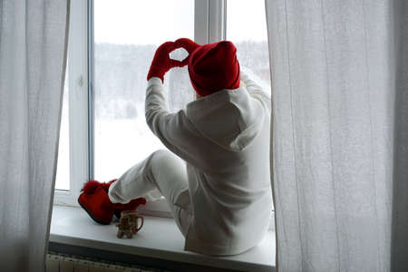 A woman in a white suit sits on the windowsill and looks out the winter windowの写真素材
