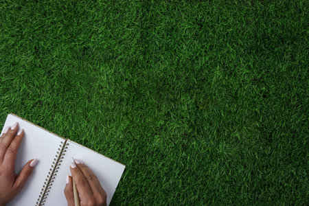 A person writing on a notebook on a field of grassの写真素材