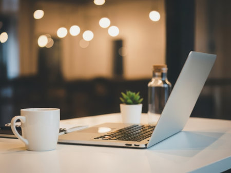 A cozy workspace featuring a laptop, a cup of coffee, and a small potted plant on a table.の素材