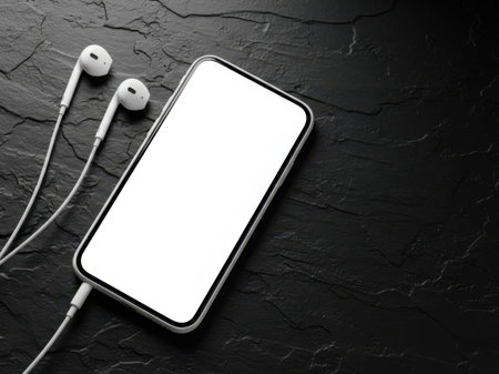 Modern smartphone with white earphones on dark surfaceの素材