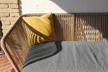 brown rattan terrace sofa with gray mattress and yellow pillow and stripes of shade from the sun...