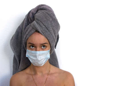 young white woman with gray towel in the head and blue medical mask on the white background. home spa, space for text, close upの写真素材