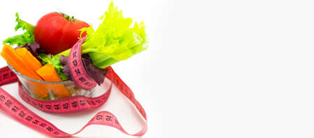 Concept of weight loss, a bowl with fresh vegetables with pink measuring tape on white background. horizontal photograph. Close up. space for text. bannerの写真素材
