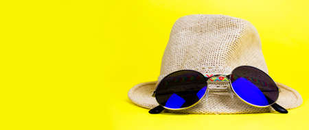 Womens summer straw hat with a brim, blue rounded sunglasses on yellow background side view copy space. Banner.の写真素材