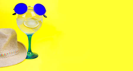 gin tonic on crystal glass with lemon slice, summer hat and little round sunglasses on yellow background. Space for text. Bannerの写真素材