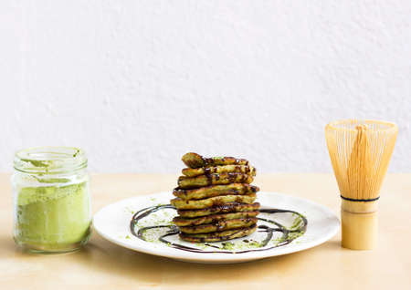 Matcha tea green pancakes. Pile of homemade pancakes with chocolate and powred matcha between glass jar of green matcha powder and Bamboo Matcha Whiskの写真素材