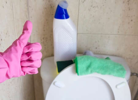 female hand with pink rubber gloves shows a thumbs up (super) in the toilet on the background of a...