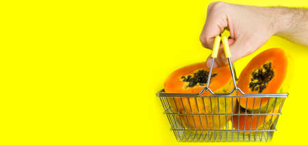 Shopping basket with tropical fruit papaya and man hand holding the basket on yellow background....
