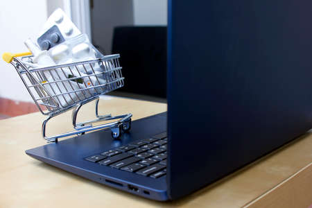 Close up Laptop and pills in small shopping trolley. Online Pharmacy. Drugs delivery. Online shopping. Stay home. Order Supplements and medications At An Online Pharmacyの写真素材