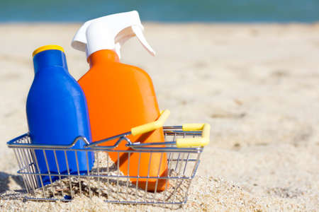two bottles of sunscreen lotion or cream with spf on the sandy beach in a small metal yellow...