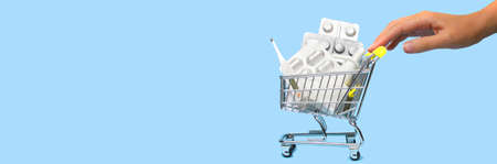 Side view of a woman hand pushing and rolling a mini shopping cart full of pills. The concept of online shopping medicine on blue background. Online Pharmacy. health insurance. Banner. Space for textの写真素材