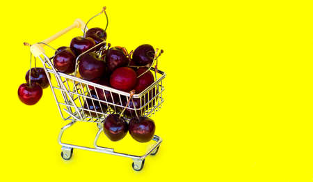 Grocery shopping cart or mini trolley with cherry. Online shopping concept. Buy food and fruits online with fast delivery. Yellow background with space for textの写真素材