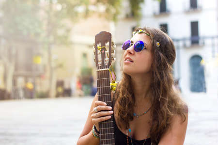 Beautiful young curly hair hippie woman with rounded vontage blue sunglasses sitting on a bench in the squareの写真素材
