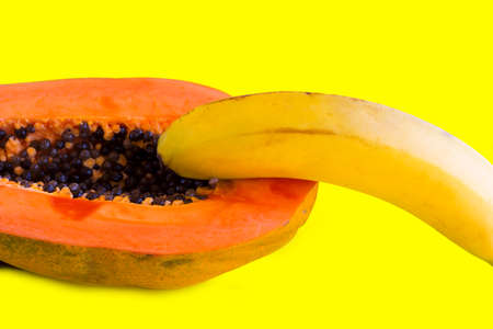 Half of sweet papaya with seeds and banana on it on yellow background. Erotic and sex concept.の写真素材