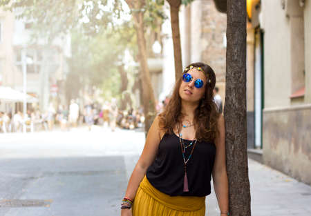 Beautiful curly hair brunette hippie girl with vintage blue sunglasses and guitar sitting on a...