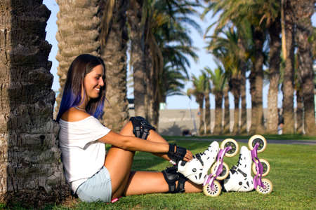 Young happy cheerful brunette roller skates girl with blue hair and roller protection tighten the...