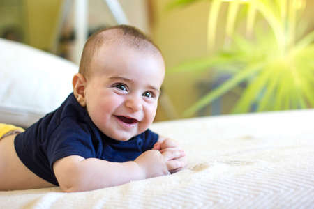 Cute Smiling baby boy with blue T-shirt in white sunny bedroom with green plant. children, people,...