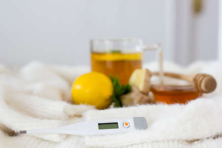 Selective focus on thermometer on light background. Cup of tea, lemon, mint, ginger root and honey...