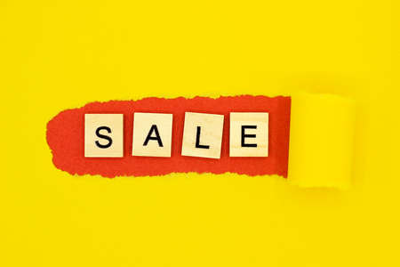 Wooden letters shaped word SALE on red background on torn yellow paper. The discount season is open. Time for a sale. Space for textの写真素材