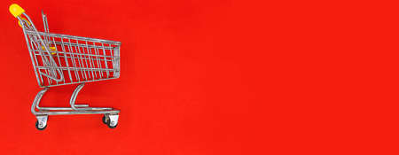 A yellow mini empty shopping trolley on red background with space for text. banner. Online shopping...
