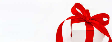 Close up white gift box with red ribbon and bow on a white background. Space for text. Banner