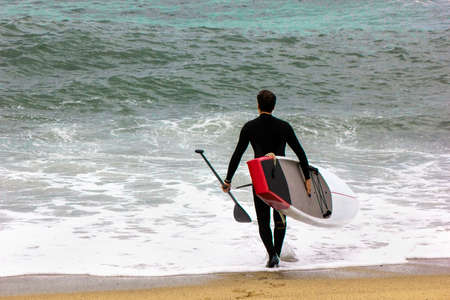 Man With Sup Stand Up Board Going To The Sea. Paddle surf boarding. Active lifestyle water sports conceptの写真素材