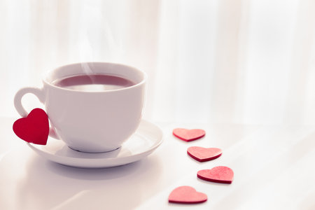 Romantic tea party for lovers on Valentines day. Red heart shaped figurins with white cup of tea on light background. Good morning with hot tea concept. Space for text. tonnedの写真素材