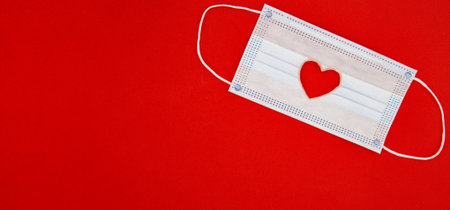 Medical protective face mask with red heart shape on red background. Valentines Day concept, stay safe. cut out heart shape Flatlay Top view. Space for textの写真素材