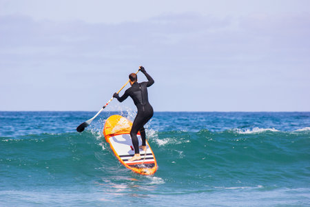 Man surfing on inflatable stand-up paddle board at summer sunny day. Extreme sport activity. Surfer caught the waveの写真素材