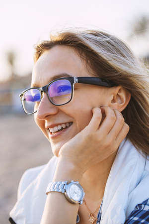 Young blond woman at the beach on a cold day. Portrait of Cheerful Woman with glasses. Vertical photoの写真素材