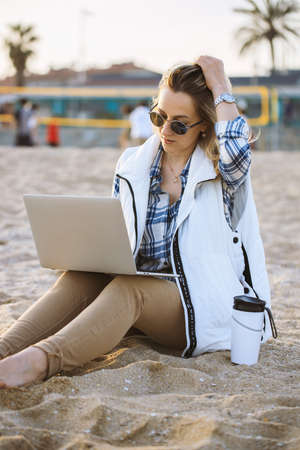 Freelance Woman Working In Vacation with laptop on the beach. Woman with sunglasses winter beach. Empty beachの写真素材