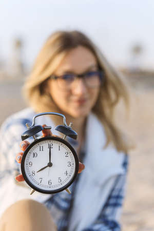 Selective Focus on the clock. Clock on the morning beach, blurred young business woman on background. Freelance, time management concept. Stress at Workの写真素材