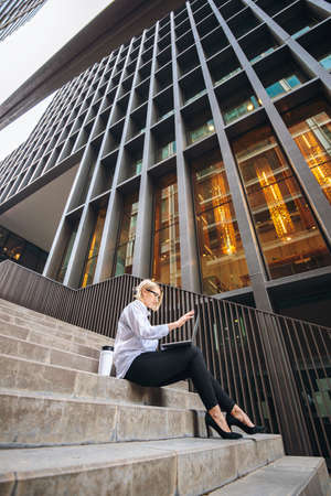White collar businesswoman working with coffee and laptop on the steps of a high-rise building. Successful woman. Freelanceの写真素材