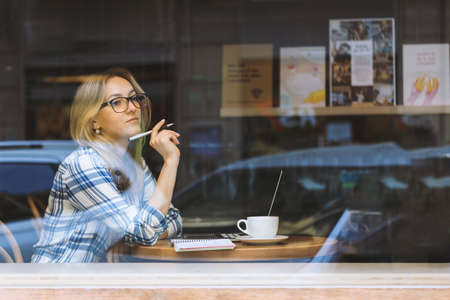 Young beautiful woman working in a cafe and thinking. Online courses. Freelance, new normal working....