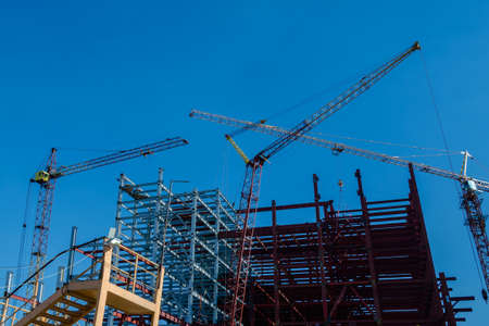 A building under construction and the construction cranes on a blue sky backgroundの写真素材