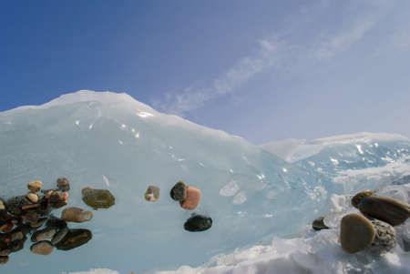 Clear ice of lake Baikal with small stones on blue sky background.