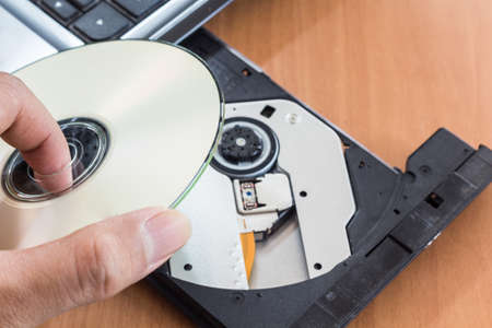 hand holding Disk insert to laptop computerの写真素材