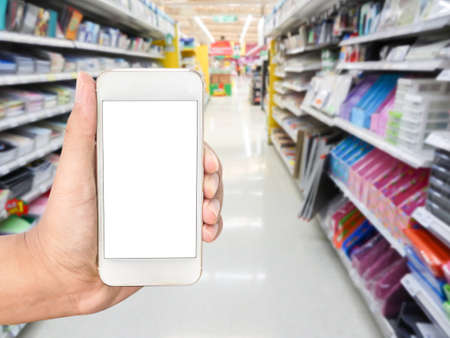 Hand holding mobile smart phone on Office supply shelf in store blur backgroundの写真素材