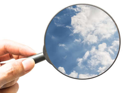 Hand holding magnifying glass with blue sky isolated on white backgroundの写真素材