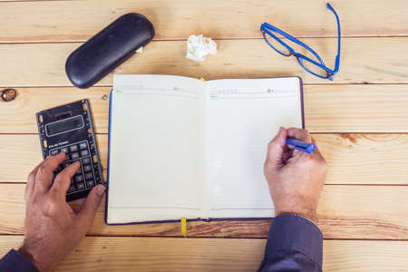 Male hands with calculator and notebook on wooden tableの写真素材
