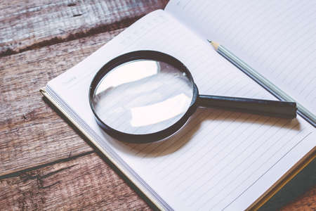 Magnifying glass and  notebook on wooden tableの写真素材