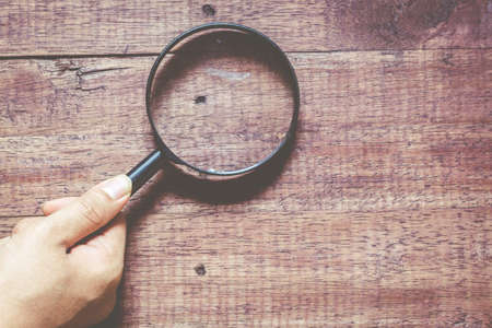 Hands with magnifying glass on the  wooden backgroundの写真素材