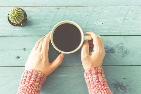 Female hands holding cup of coffee on wood tableの写真素材