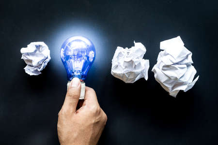 Hand holding light bulb with crumpled office paperの写真素材
