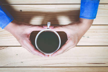 Hands with cup of coffee on wooden tableの写真素材