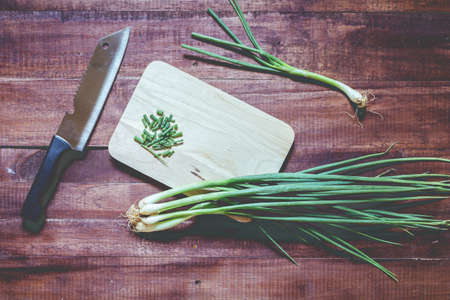 Green onions with Knife on chopping board on wooden backgroundの写真素材