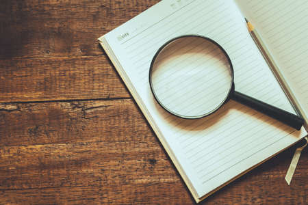 Magnifying glass and  notebook on wooden tableの写真素材