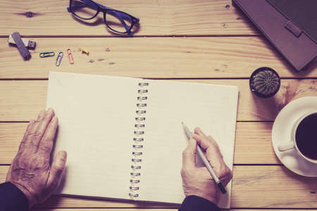 Hans writing on a wooden table with office suppliesの写真素材