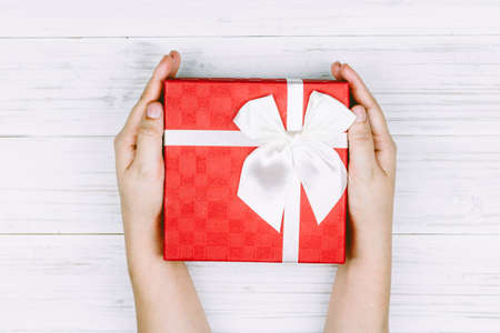 Hand holding red gift box with ribbon on wooden background